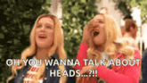 two blonde women are laughing and one of them is covering her face with her hand .