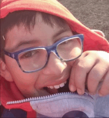 a young boy wearing glasses and a red hoodie is biting a zipper