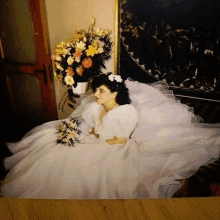 a bride in a wedding dress is sitting on a bed with a bouquet of flowers .