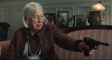 an elderly woman is holding a gun in front of a couch