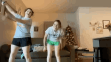 two girls are dancing in a living room with a christmas tree in the background .