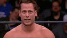 a man without a shirt is standing in a ring with a crowd behind him