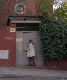 a woman in a white coat is standing in front of a building with a sign that says ' m + ' on it