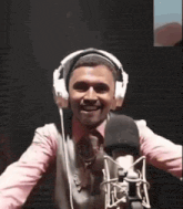 a man wearing headphones is standing in front of a microphone and smiling .