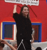 a woman is standing in front of a red sign that says `` kitchen and sofas for friends '' .