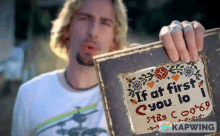 a man is holding a cross stitch that says " if at first you lo stay cool "