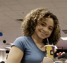 a woman in a blue shirt is smiling while holding a cup that says mcdonald 's