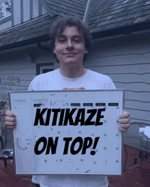 a young man holds a sign that says " kitikaze on top "