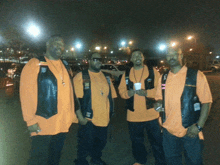 a group of men wearing orange shirts and black vests stand together