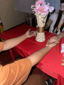 a vase of pink flowers sits on a table with two people holding hands