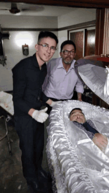 two men are standing next to a coffin with a man laying in it