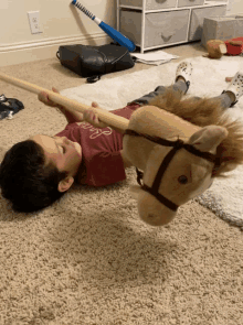 a young boy laying on the floor playing with a stuffed horse and a baseball bat