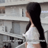 a woman with long black hair is standing on a balcony with the caption " tocate el pelo si eres de venus " written below her