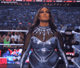 a woman in a silver and black outfit is standing in a wrestling ring ..