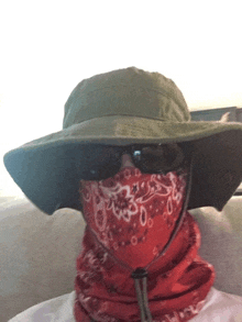 a man wearing a green hat and sunglasses has a red bandana around his neck