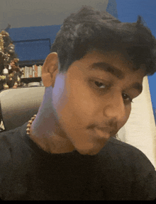 a young man with a necklace around his neck looks at the camera with a christmas tree in the background