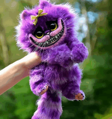 a person is holding a stuffed purple cat with a bow on its head