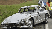 a silver car with a broken windshield is parked in the grass