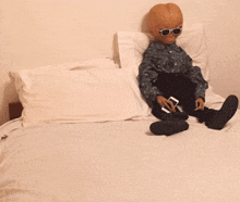 a doll with sunglasses is sitting on a bed