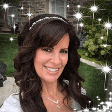 a woman wearing a headband and a necklace smiles in front of a house