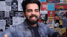 a man with a beard is smiling and giving a thumbs up in front of a wall covered in posters