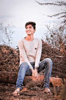 a young man is sitting on a log with his legs crossed and smiling