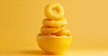 a bowl of onion rings stacked on top of each other on a yellow background