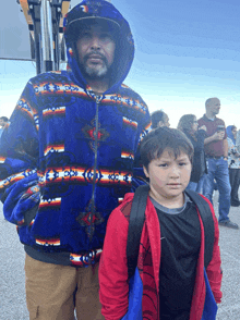 a man in a blue jacket stands next to a boy in a red jacket with a backpack