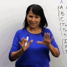 a woman in a blue shirt is holding a marker in front of a whiteboard with the letters a through i written on it