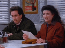 a man and a woman are sitting at a table in front of a coca-cola sign