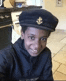 a young boy wearing a black hat with an anchor on it is smiling for the camera .