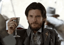 a man with a beard is holding a glass of wine and looking at the camera .