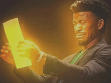 a man in a suit is crying while holding a piece of paper with a yellow light coming out of it