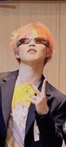 a man with pink hair and sunglasses is making a peace sign with his hands .