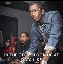 a man in a denim jacket is looking at a computer screen with a caption that says " in the office looking at data like "