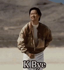 a man in a jacket is standing in the desert with the words `` k bye '' written on his face .