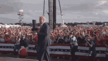 a man in a suit and tie is walking in front of a crowd with a sign that says ' donald trump ' on it