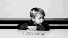 a black and white photo of a young boy sitting at a table with his hands on his hips .