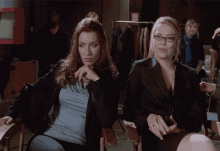 two women are sitting in chairs and one has glasses