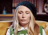 a woman wearing a black hat and a green vest is sitting in a chair .