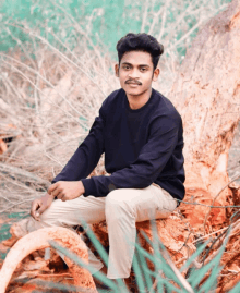 a young man in a black shirt sits on a log