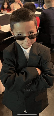 a young boy wearing sunglasses and a suit is standing with his arms crossed