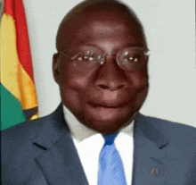 a man wearing glasses and a suit and tie is smiling in front of a flag .