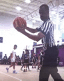 a referee is holding a basketball in his hands while a basketball game is going on .