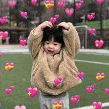 a little girl is making a heart shape with her hands on her head surrounded by hearts .