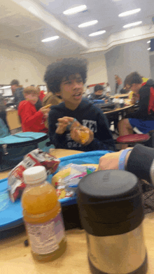 a boy sitting at a table with a bottle of orange juice