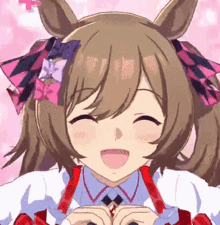 a close up of a girl with pigtails and a bow on her head making a heart shape with her hands .