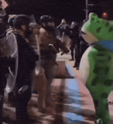 a green frog mascot is standing in front of a crowd of people .