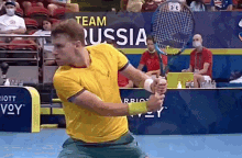 a man in a yellow shirt is holding a tennis racquet in front of a sign that says team russia