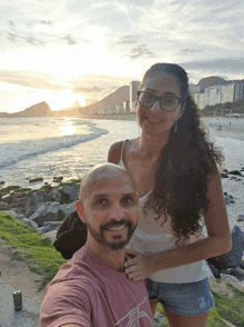 a man and a woman are posing for a picture on a beach with a can of beer in the foreground